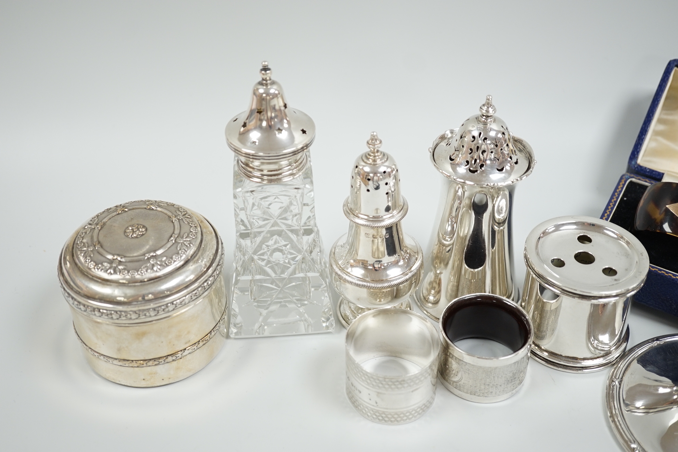 A group of mixed silver including three sugar casters, two inkwells, two pairs of napkin rings (one tortoiseshell) and a white metal box and cover.